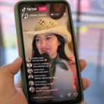 Celular exibindo uma live no TikTok com Silvana França cantando ao microfone, usando chapéu de palha e lenço verde.