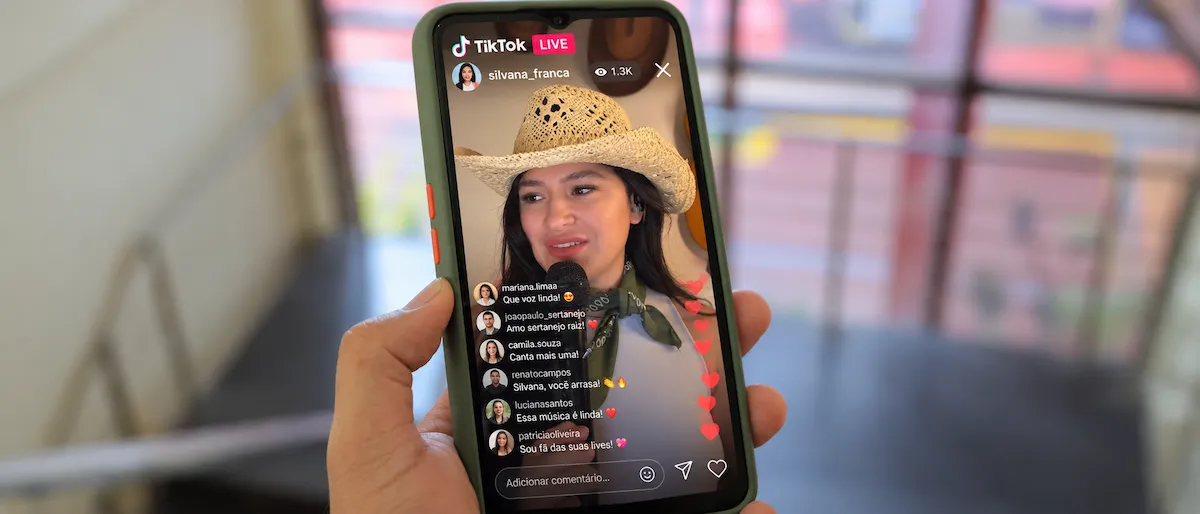 Celular exibindo uma live no TikTok com Silvana França cantando ao microfone, usando chapéu de palha e lenço verde.